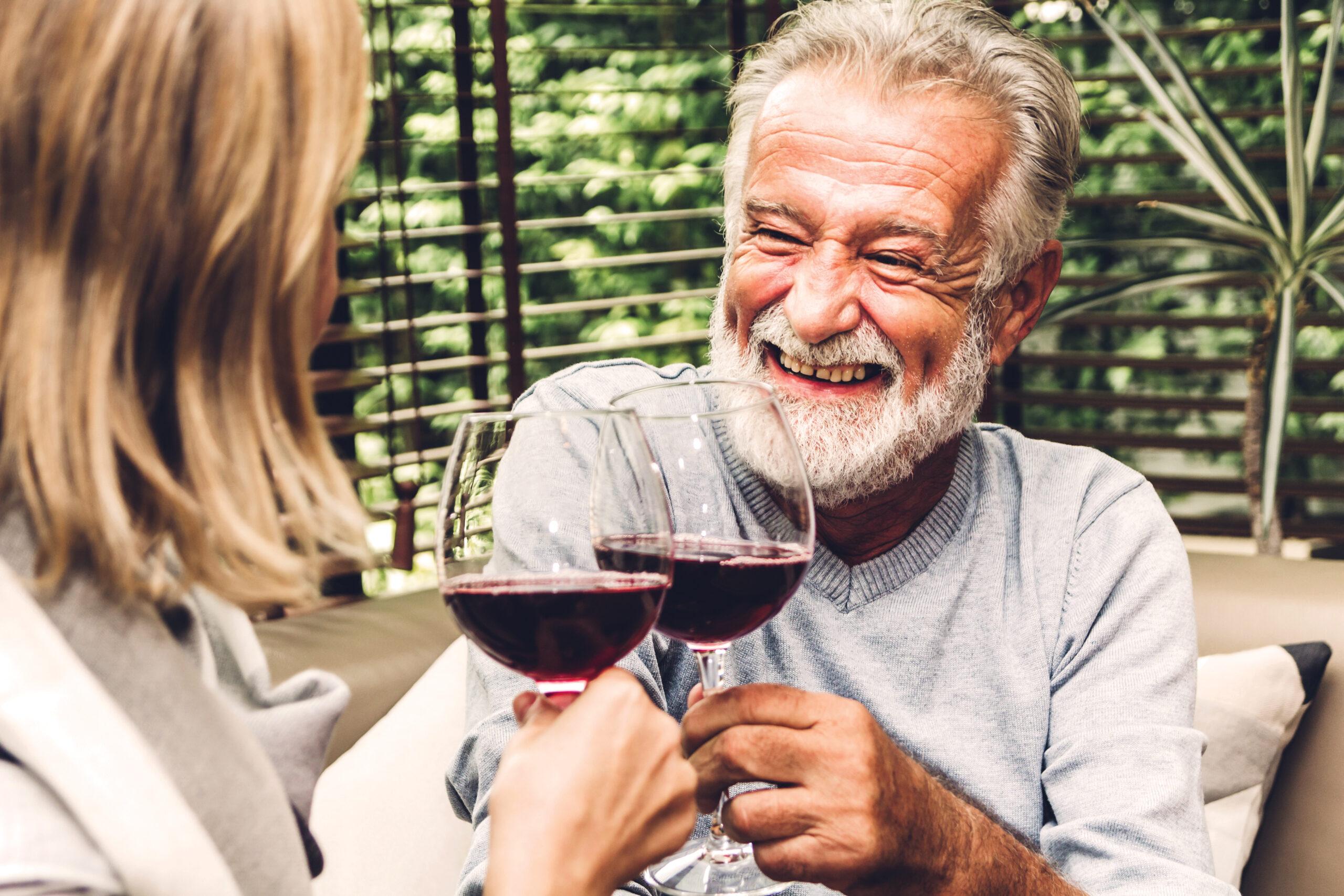 Senior couple smiles and laughs over glasses of wine