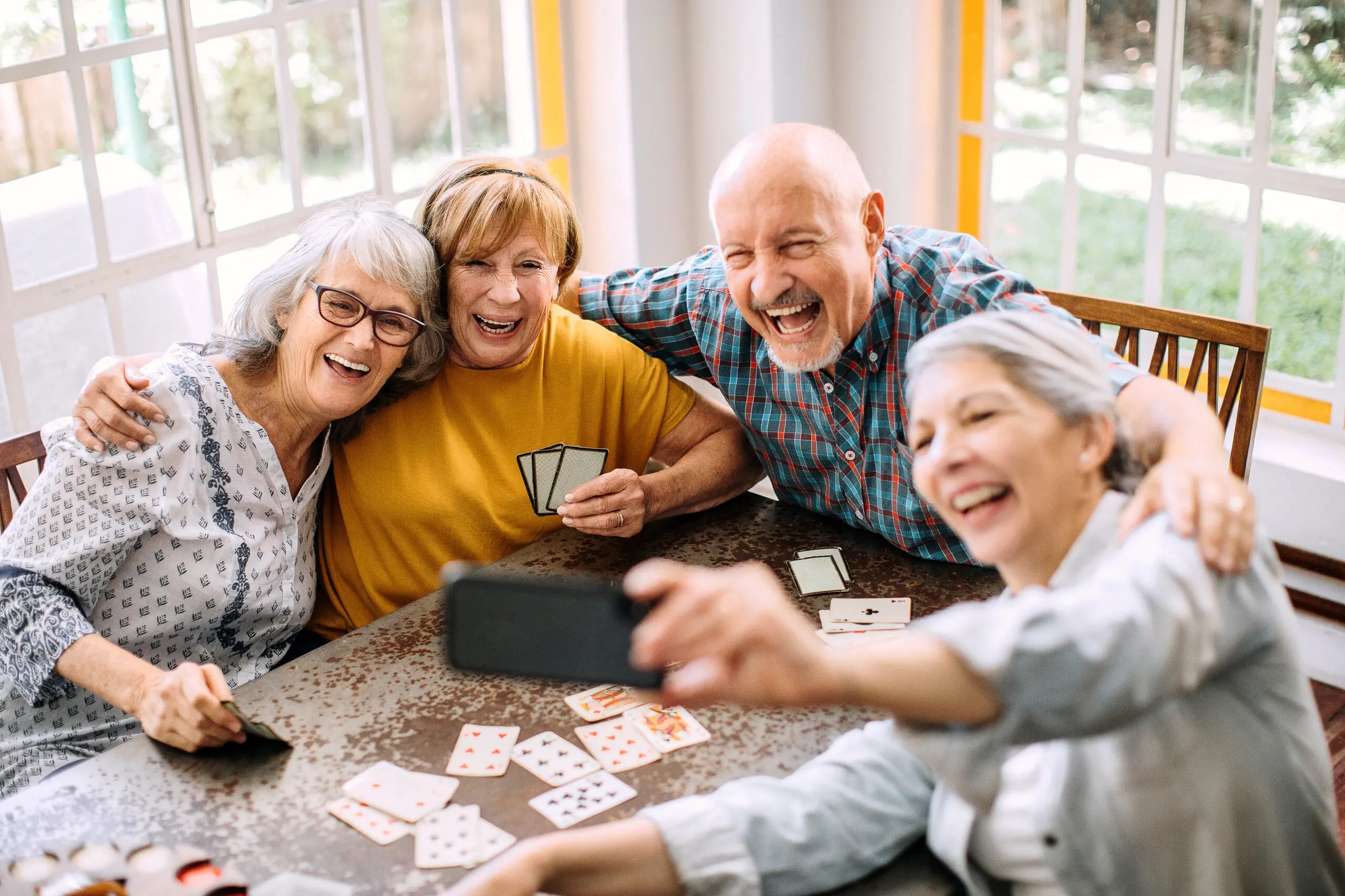 Seniors smile and laugh for a selfie while playing cards