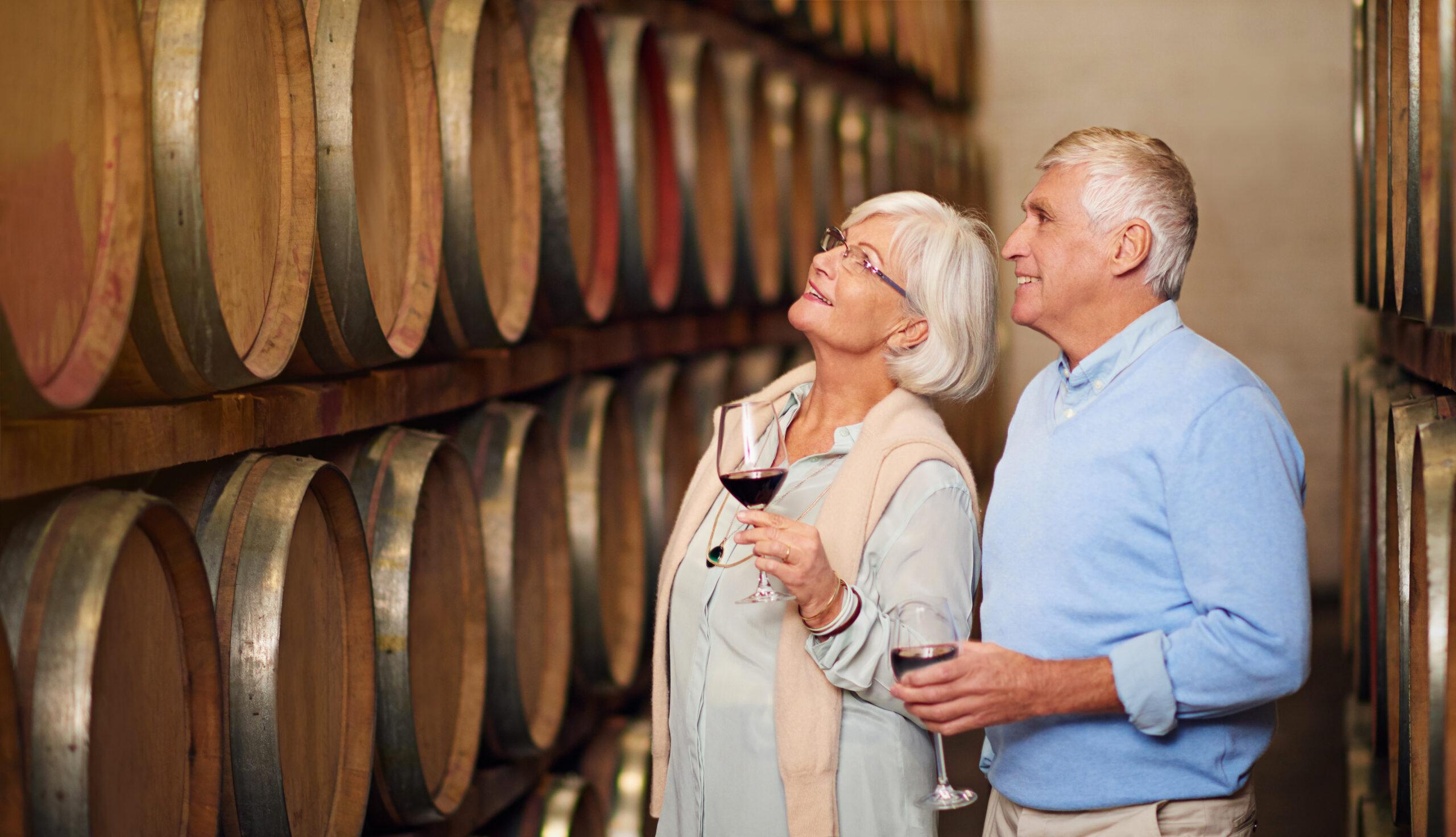 Affectionate senior couple holds wine glasses and views a wine cellar